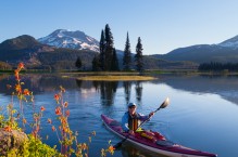 Woman kayaker paddles on Sparks Lake, Oregon, with red columbine in foreground and South Sister behind (MR).