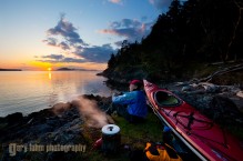Male sea kayaker enjoying hot tea and sunset while camping on Jones Island, San Juan Islands, Washington State (MR).