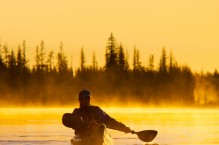 A woman in a sea kayak paddles at dawn on Big Lake, Oregon.