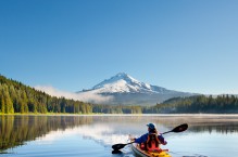A woman in a sea kayak paddles at dawn on Big Lake, Oregon.