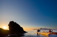 Two women sea kayakers paddling at dawn at Doe Island, San Juan Islands, Washington State.(MR)