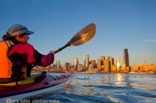 Woman sea kayaker paddling toward downtown Seattle at sunset, Elliott Bay, Washington State.