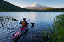 A woman in a sea kayak paddles on Trillium Lake, Oregon, in the Oregon Cascades, with a Mt. Hood backdrop.