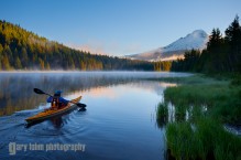 A woman in a sea kayak paddles on Trillium Lake, Oregon, in the Oregon Cascades, with a Mt. Hood backdrop.