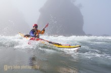 Sea kayaker launches through mild surf at Point of Arches, Olympic National Park, Washington State.