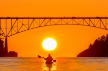 Woman sea kayaker paddles beneath the Deception Pass Bridge.