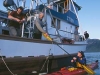 Captain Jim Kyle hands paddle to guest as Ben Kyle looks on, Southeast Alaska.