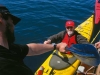 Jim and Ben Kyle. Kayak guide and first mate Ben Kyle hands a paddle to Captain Jim of the Home Shore, from the launch platform.