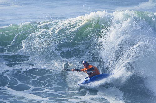  From the cliff: The world is flat. High perspective, backlit,  waves break away from the photographer. A 12-footer made small. 500mm f/4 w/1.4x, f/5.6, exposure unrecored, Fuji Provia 100  What got me going on this was a matter of perspective—what angle, what position, what elevation, what field of view or lens choice would yield a worthy photograph. It was pretty obvious that photographing kayak surfing—or surfing generally—at Steamer Lane from the cliff had disadvantages. Plenty of photographers there do it, often with a super-telephoto 600mm f/4 or even a 400mm f/2.8 lens. I have a 500mm f/4, almost as good but hard to compete with the bigger guns (the 400m f/2.8 with a doubler gets you an 800mm f/5.6; the 600mm f/4 w/1.4x is a 840mm f/5.6. If I put a 1.4x on my 500mm f/4, I get a 700mm f/5.6). The cliff-side photographers also seem willing to spend all day shooting. If this yields great stuff, how can you compete? Well, their problems abound. The cliff at Steamers faces southeast, so in the sweet morning light images from the cliff will be backlit, and that continues through much of the day. Then you’re shooting down on the surfers, flattening the waves and making big waves appear small. In the afternoon if the tide is low, it’s possible to shoot frontlit from the beach below the cliffs as the sun descends to the west, but that just exemplifies a third problem. The waves break away from you as they bend around the point, scratching any chance of getting a kayak surfer wrapped in the energy-pumping curl of a breaking wave. You can shoot all day from cliff-side, and never—putting it bluntly—get the shot.  From the kayak: The world excites. Rich, warm morning light; front-lit; engaging perspective.  The waves may be small, but the low angle pumps them up. A four-footer looms large.  300mm f/4 w/1.4x, f/6.3, 1/2000sec, ISO 400     